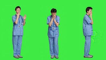 Medical assistant feeling extremely sleepy against greenscreen backdrop, being overworked after the night shift. Woman nurse yawns and feels exhausted in studio, burnout and anxiety. Camera A. photo