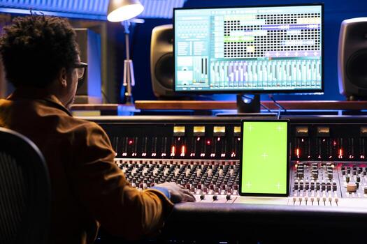 Audio engineer editing music on control desk panel board, recording tracks to add sound effects in post production. Technician producer looks at device with mockup layout in studio. photo