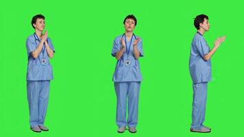 Smiling medical assistant applauding someone in studio, celebrating success and cheering against greenscreen backdrop. Young nurse clapping hands and feeling happy about achievement. Camera A. photo