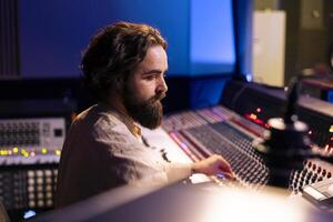 Sound producer working on mixing and mastering sounds with pc software, editing music with audio console mixer station. Skilled audio technician creating tunes in professional recording studio. photo