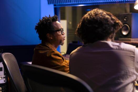 Team of musician and producer working on composing a song together, does mixing and mastering with faders and buttons. Artist collaborating with technician creating tracks in control room at studio. photo