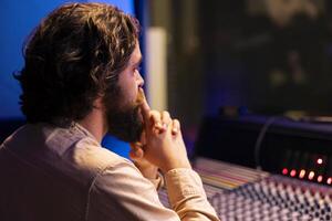 Music engineer working on mixing and mastering tunes with digital software, editing music with audio console control desk. Skilled sound technician creating tracks in professional studio. photo