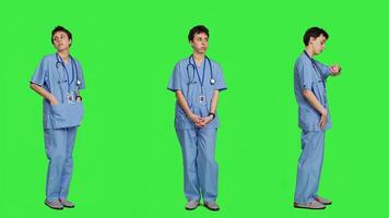 Stressed nurse checking time on watch and waiting for patient to arrive at checkup examination, being impatient against greenscreen backdrop. Medical assistant with scrubs and stethoscope. Camera A. photo
