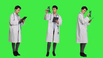 General practitioner studying radiography scan results for patients with disease, stands against greenscreen backdrop. Medic examines x ray diagnosis, works with a tablet. Camera A. photo