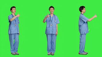 Cheerful nurse giving thumbs up sign against greenscreen backdrop, showing positive gesture with a like. Medical assistant shows her approval, recommending something and being satisfied. Camera A. photo
