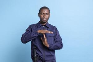 Patrol agent showing a timeout gesture against blue background, asking to take a break while he is on protection duty. Staff in bodyguard uniform showing a pause symbol to relax. photo
