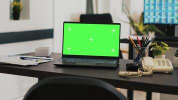 Office with green screen laptop on desk and monitor in background with stock exchange listings. Mockup notebook in workspace and computer screen in background displaying trading platform photo