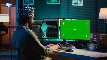 IT admin coding and using EEG headset to upload brain into mockup computer, gaining immortality. Neuroscientist engineering transhumanism experiment on isolated screen PC, camera A photo
