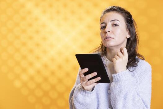 Portrait of woman intrigued by interesting ebook on ereader, conveying joy of reading concept, studio background. Geek enthralled by compelling digital novel plot twists on tablet screen photo
