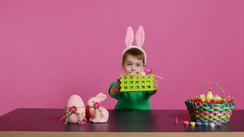 Sweet young boy making colorful arrangements for Easter holiday festivity, putting painted eggs in a handcrafted basket. Ecstatic joyful kid using crafting materials to create decorations. Camera B. photo