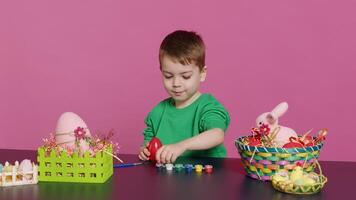 Small sweet child decorating eggs with stamps and watercolor, preparation for easter sunday holiday. Joyful little boy having fun coloring festive decorations, painting designs in studio. Camera A. photo