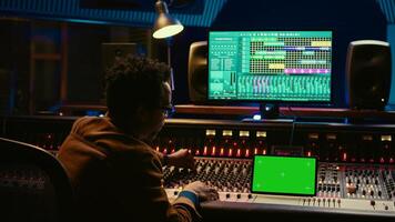 Professional audio technician recording tracks with mockup on tablet, creating tunes on mixing console to add on songs in post production. Engineer pressing buttons, process sounds. Camera B. photo