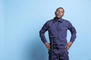 Security officer on patrol showing his authority in front of the camera, standing with hands on his hips against blue background. Serious confident agent in studio, proud of his work duty. photo