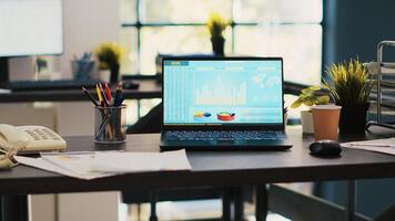 Stock market diagrams with charts and stock figures on laptop showing profits, empty workspace. Trading index listings displayed on notebook screen in office, panning shot photo