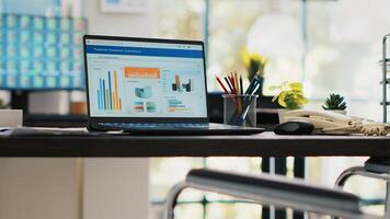 Wheelchair in inclusive office for employees and laptop on desk showing statistics. Medical chair in workspace offering accessibility to workers with disability and notebook with financial charts photo