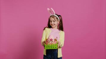 Smiling pleased girl presenting her handcrafted easter basket filled with painted eggs and other festive decorations for holiday celebration. Joyful small kid proud of her arrangement. Camera B. photo