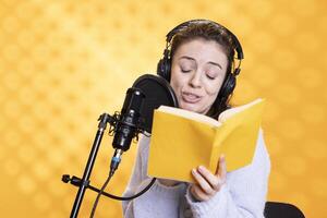Voice actor reading book, recording audiobook using microphone and headset, playing character, studio background. Woman using mic to produce digital recording of novel, doing dramatic acting photo