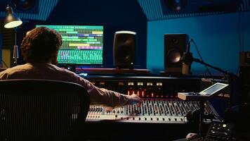 Tracking engineer processing and mixing sound on audio console with moving faders and colored meters. Music producer working on a new album, creating a hit song in studio. Camera B. photo