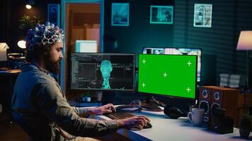 Developer using EEG headset, starting mind upload process using isolated screen desktop. Man using neuroscientific device to transfer consciousness into cyberspace with chroma key monitors, camera B photo