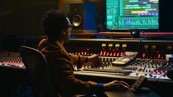 Tracking engineer processing and mixing sounds in control room with audio console and professional editing software on computer. Music production expert uses motorized faders and knobs. Camera A. photo