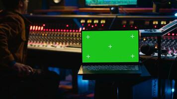 Skilled audio technician processing and mixing sounds next to mockup display on laptop, using variety on knobs, buttons and sliders to edit audio recordings and produce new music. Camera A. photo