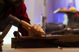 Sculptor shaping raw timber using chisel and hammer, creating wood art, making precise cuts. Artist making handmade wood sculptures, engraving lumber with tools, close up shot photo