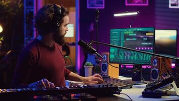 Sound engineer pressing keys of electric synthesizer and recording new music, adjusting noise level. Artist singing song on microphone, works with mixing board in home studio. Camera A. photo