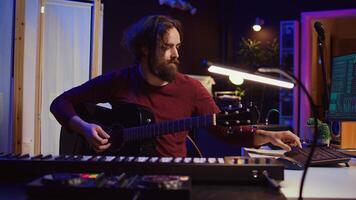 Artist working with daw software at his home studio to record new music on mixing console and soundboard, audio engineering. Musician playing song on guitar and adjusting volume. Camera B. photo