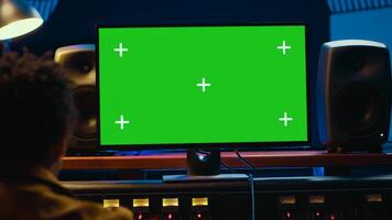 African american audio engineer uses greenscreen on pc in professional recording studio, working with mixing console and twisting knobs to edit tracks. Music producer creating tunes. Camera A. photo