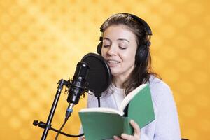 Cheerful voice actor reading book, recording for audiobook production using microphone and headset, studio background. Happy person using mic and headphones to produce digital recording of novel photo