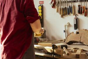 Man in studio with woodworking tools in background using sandpaper for sanding wooden surface. Woodworking expert using abrasive sponge to fix damages suffered by piece of wood photo