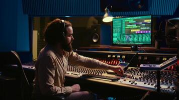 Mixing engineer pressing sliders on control desk to balance tracks and add sound effects, creating new music. Audio engineering expert works with motorized faders in professional studio. Camera B. photo