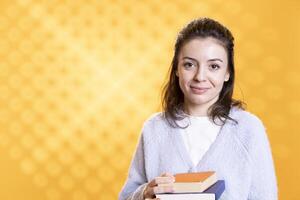 Portrait of smiling woman holding pile of books, enjoying reading hobby for entertainment purposes. Cheerful bookworm with stack of novels in arms enjoying leisure time, studio background photo