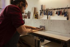 Woodworker wearing safety glasses operating spindle moulder to create bespoke joinery for client commissioned project. Manufacturer performing tasks on wood shaper, shaping and cutting planks photo