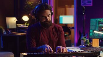 Young artist composing a song on electronic piano keyboard at home recording studio. Audio engineer playing MIDI controller, working on producing a soundtrack, soundboard tools. Camera A. photo