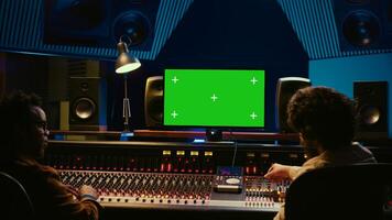 Team of music engineer and artist recording tracks on greenscreen, processing sounds to create a new song. Musician working closely with producer to make high quality tunes. Camera A. photo