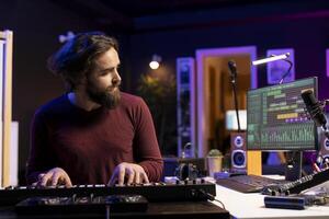 Music producer playing electronic piano keyboard in home studio, recording midi controller notes to create new songs. Young artist producing synthesizer keys, post production techniques. photo