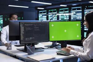 Colleagues working on green screen desktop PC in data center housing storage infrastructure. Coworkers using mockup computer display in server hub workspace filled with networking tech photo