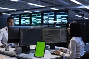 Team of programmers in data center using isolated screen tablet to check for server issues arising due to high CPU usage. Server hub teamworking colleagues fixing errors with mockup device photo
