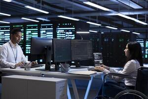 Person with disability and coworker in inclusive server room facility ensuring data remains shielded from threats. Wheelchair user and colleague protecting data center hardware equipment photo