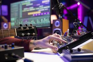 Sound engineer using mixing console and acoustic guitar in home studio, adjusting volume levels in post production editing. Music producer creating soundtracks, twisting pre amp knobs. photo