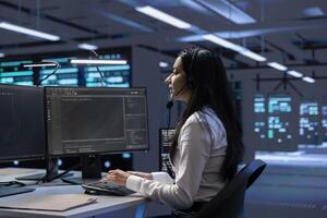 Data center support expert supporting engineering team doing equipment maintenance, talking in headset microphone. Woman in server farm coordinating technicians using mic photo