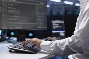 IT administrator working on PC in hardware room housing server rackmounts, storage devices and networking units providing vast amounts of computing resources, doing equipment maintenance, close up photo