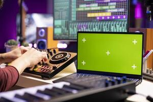 Sound engineer twisting pre amp knobs on mixing console in home studio, using laptop with greenscreen template. Music producer editing soundtracks, stereo equipment on daw software. photo