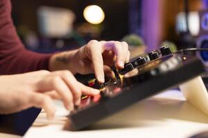 Young artist creating new music in editing post production, twisting pre amp knobs on mixing console. Skilled composer singer adjusting volume levels in post production. Close up. photo