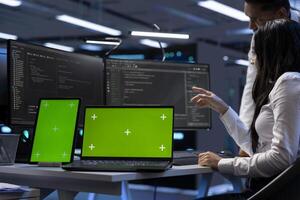 Engineers in data center using mockup tablet and laptop to check for server issues arising due to high CPU usage. Server hub workers fixing insufficient memory errors with green screen devices photo