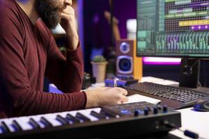 Musician composing new song in his home studio and taking notes, writing down lyrics before recording the tunes. Songwriter producing music with daw software tools and creativity. photo