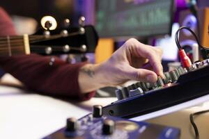 Audio engineer working with stereo equipment and control panel board, mixing and mastering tunes in his home studio. Composer singer recording soundtracks and editing in post production. Close up. photo