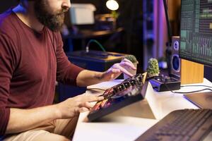 Music producer creating new tunes on mixing console by twisting pre amp knobs and adjusting volume levels in home studio. Artist songwriter working on post production with stereo gear. photo