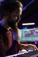 Artist thinking of new piano notes combinations to play on his electronic keyboard, recording music with daw software in home studio. Musician searching for inspiration in playing synthesizer. photo